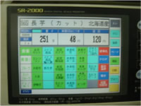 商品名をコンピューターに入力（タッチ）し、商品を乗せると、すぐに値段やバーコードがシールでプリントアウトされるシステム。それぞれの商品のデータ（加工方法、グラムあたりの単価）はすでに入力されている。（写真はAさんがカットし、袋詰めした長芋を量っている様子）