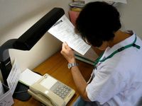 弱視のため、デスクにスタンドを置き、細かい文字を読んでいる