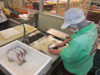 午前中の仕事：包丁で魚の下処理をしているAさん