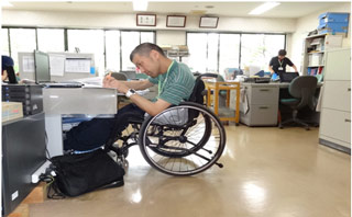 事務作業風景①車いすのまま机で事務作業出来るように机の高さを合わせている